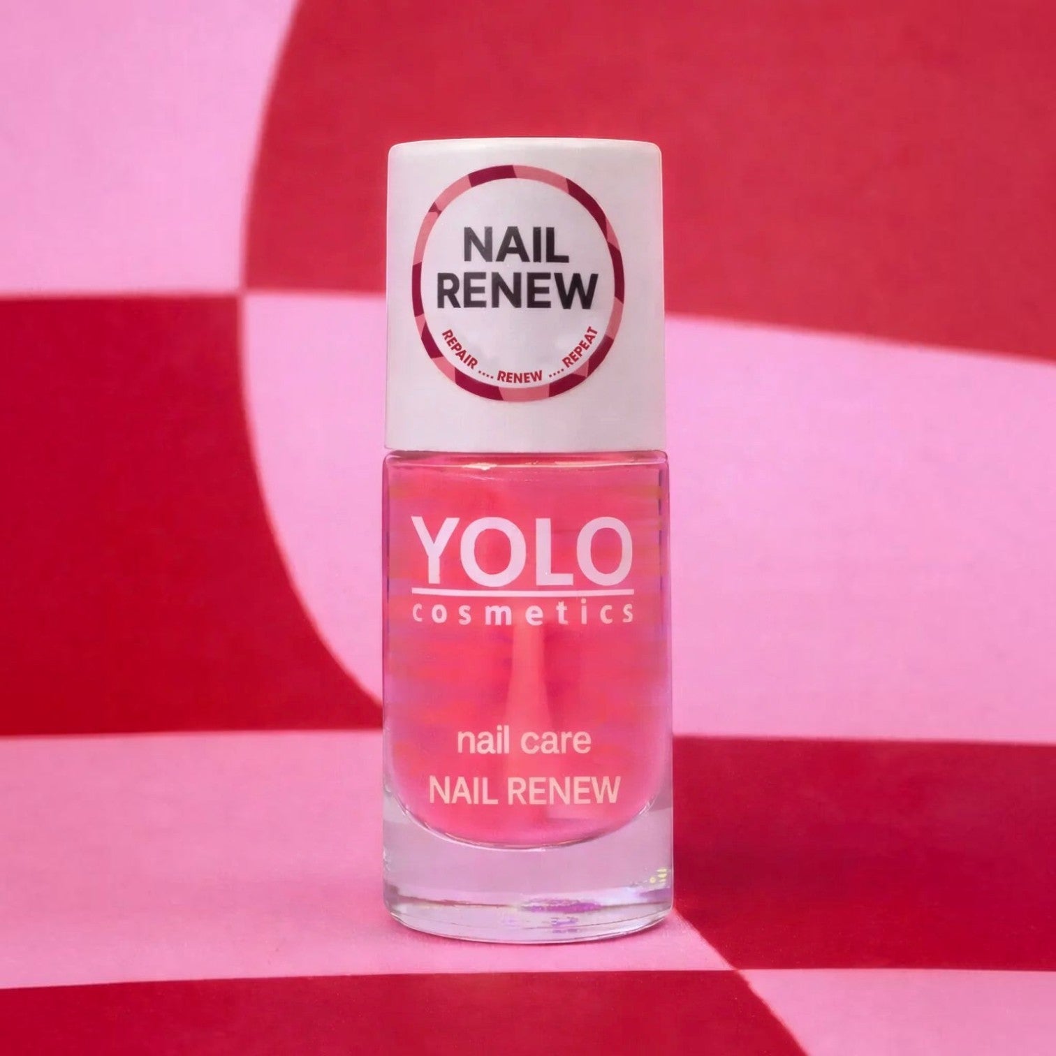 Said Salem YOLO Nail Renew strengthening serum in a clear glass bottle with a pink liquid against a checkered background